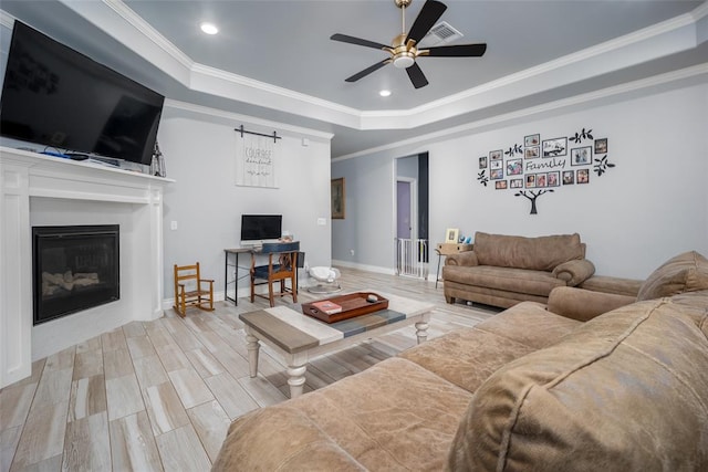 living room featuring a tray ceiling, crown molding, ceiling fan, and light hardwood / wood-style floors