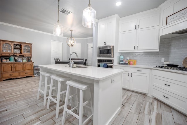 kitchen with a center island with sink, ornamental molding, appliances with stainless steel finishes, decorative light fixtures, and white cabinetry