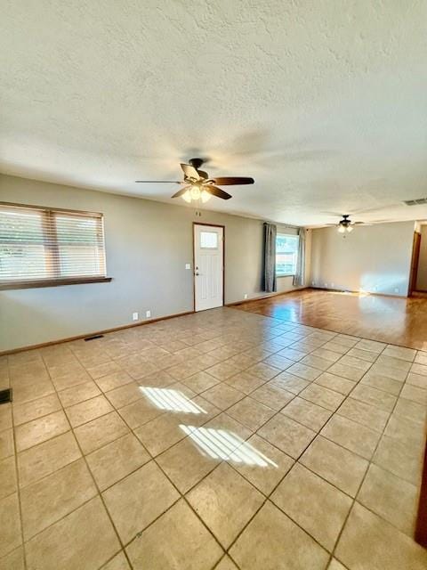 empty room with ceiling fan, light tile patterned flooring, and a textured ceiling