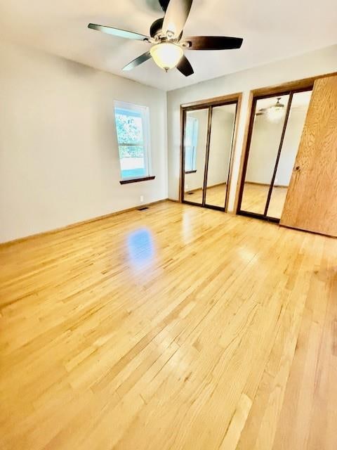 unfurnished bedroom featuring two closets, light hardwood / wood-style floors, and ceiling fan