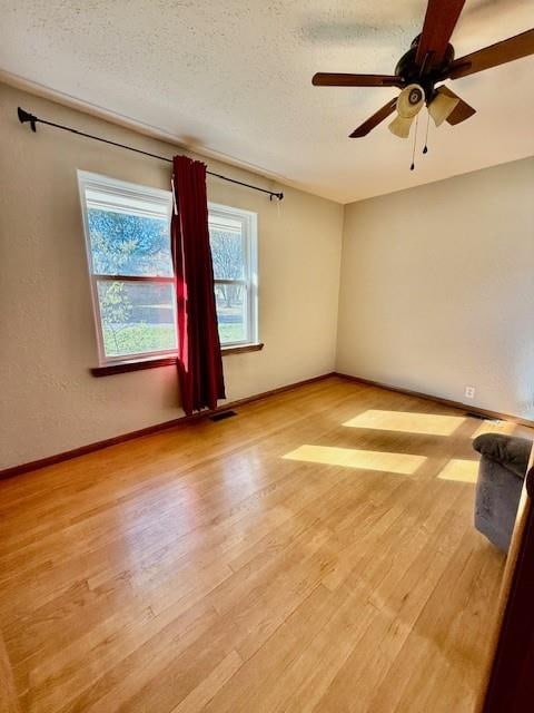 empty room featuring a textured ceiling, light wood-type flooring, and ceiling fan