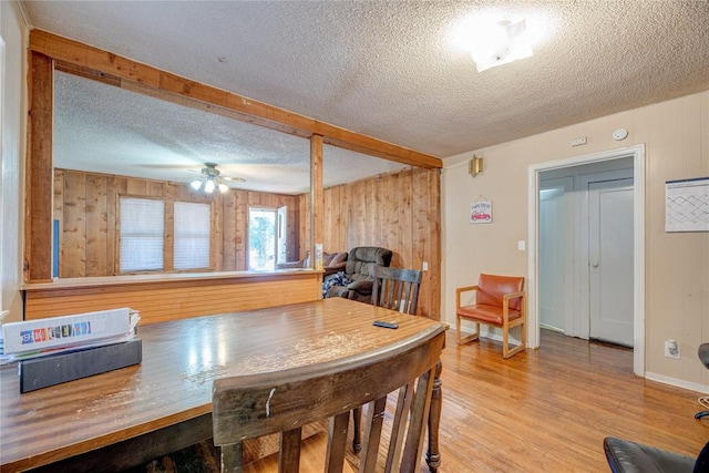 dining room with a textured ceiling, light wood-type flooring, and wood walls