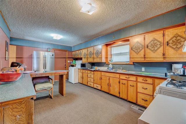 kitchen featuring sink, light colored carpet, a textured ceiling, washer / dryer, and appliances with stainless steel finishes