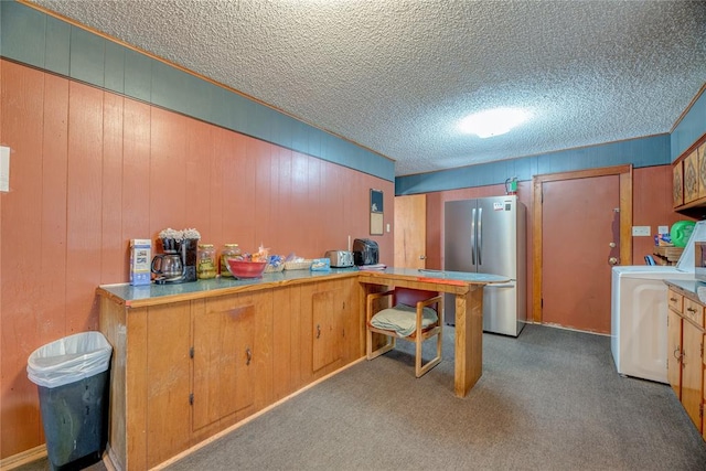 kitchen with kitchen peninsula, stainless steel fridge, light colored carpet, wooden walls, and washer / clothes dryer