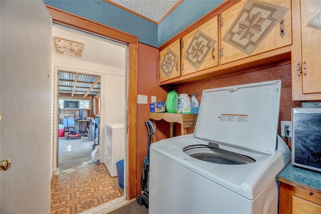 clothes washing area with cabinets, a textured ceiling, and washer / clothes dryer