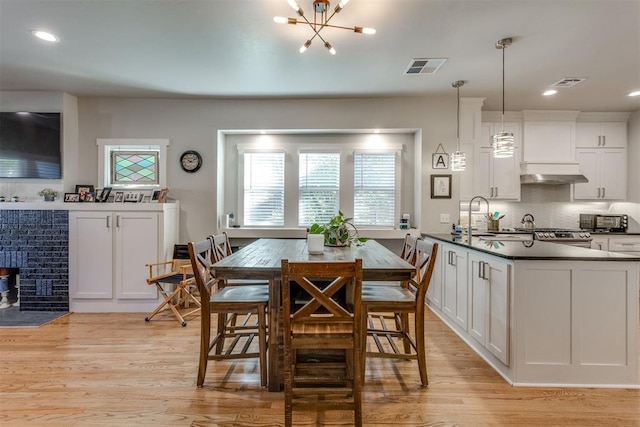 dining space with a wood stove, sink, a notable chandelier, and light wood-type flooring