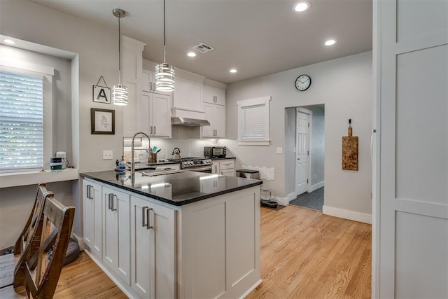 kitchen featuring ventilation hood, hanging light fixtures, light wood-type flooring, white cabinetry, and kitchen peninsula