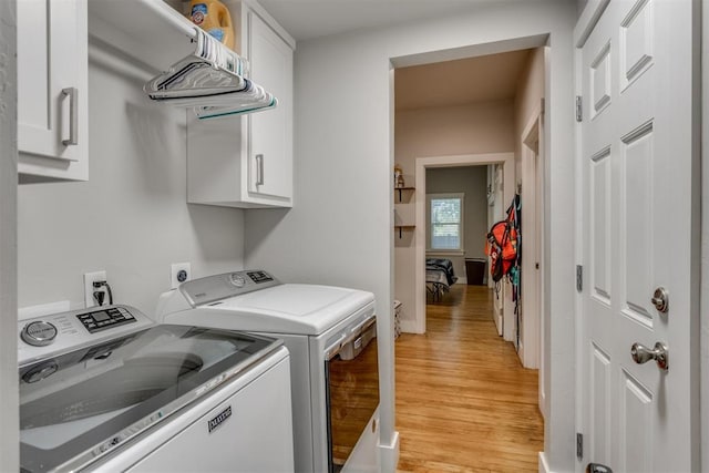 laundry area featuring washer and clothes dryer, cabinets, and light hardwood / wood-style flooring