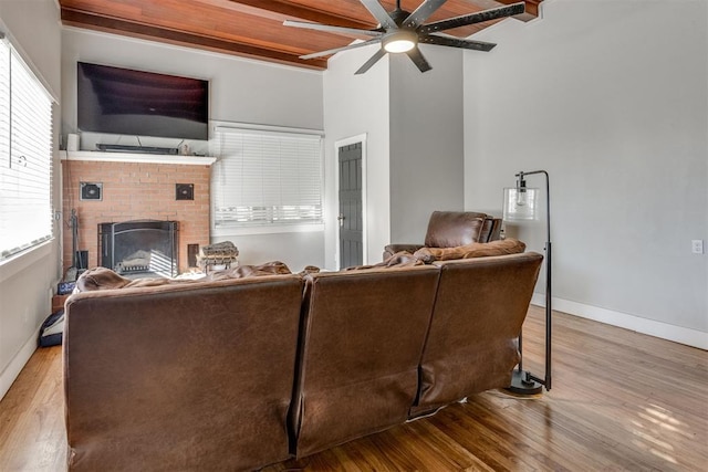 living room with beamed ceiling, wood-type flooring, a fireplace, and ceiling fan