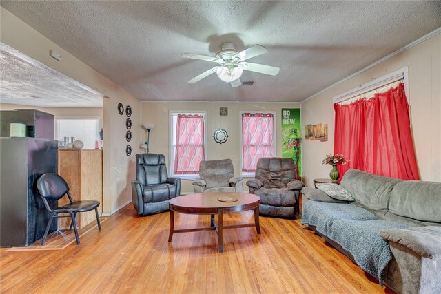 living room featuring ceiling fan, light hardwood / wood-style floors, ornamental molding, and a textured ceiling