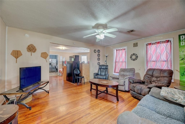 living room with ceiling fan, a textured ceiling, and light hardwood / wood-style flooring