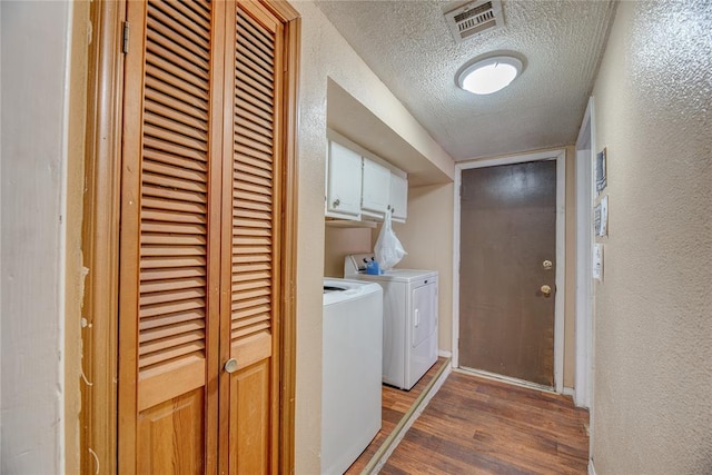 washroom featuring a textured ceiling, washer and clothes dryer, cabinets, and dark hardwood / wood-style floors