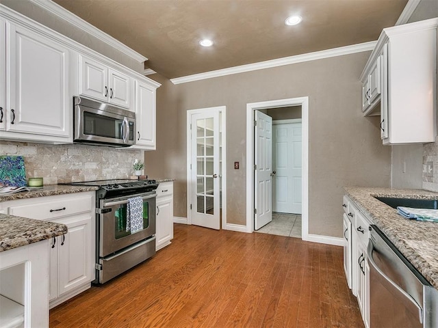 kitchen with light stone countertops, appliances with stainless steel finishes, crown molding, light hardwood / wood-style flooring, and white cabinets