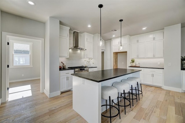 kitchen with wall chimney range hood, stainless steel gas stove, hanging light fixtures, white cabinets, and a kitchen island