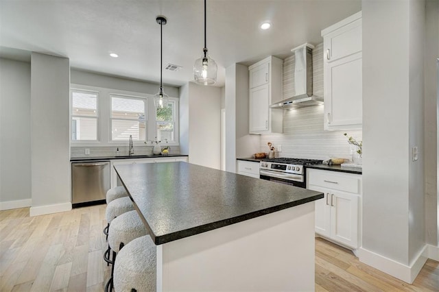 kitchen with stainless steel appliances, white cabinetry, a kitchen island, and wall chimney range hood