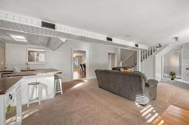 carpeted living room with sink and brick wall