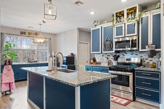 kitchen featuring a kitchen island with sink, blue cabinets, decorative backsplash, decorative light fixtures, and stainless steel appliances