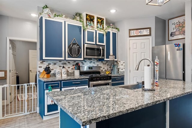 kitchen featuring backsplash, blue cabinets, sink, light stone counters, and stainless steel appliances