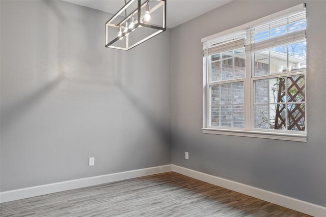 empty room with a notable chandelier, plenty of natural light, and wood-type flooring