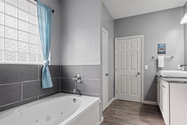 full bath featuring vanity, plenty of natural light, wood finished floors, and a whirlpool tub