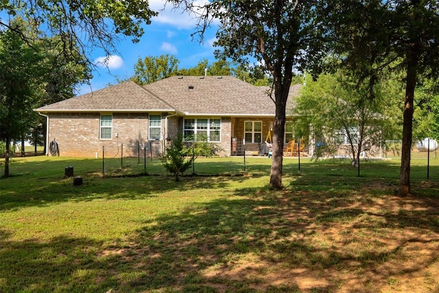 back of house with brick siding, a shingled roof, and a yard