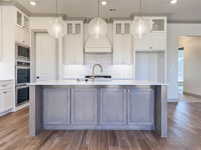 kitchen featuring appliances with stainless steel finishes, decorative light fixtures, ornamental molding, and an island with sink