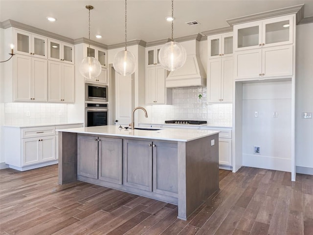 kitchen with white cabinetry, sink, stainless steel appliances, an island with sink, and custom range hood