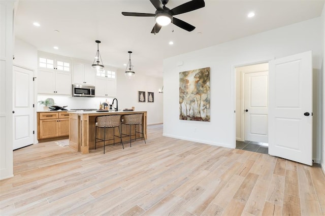 kitchen with a center island with sink, stainless steel microwave, light wood-style flooring, glass insert cabinets, and a kitchen bar