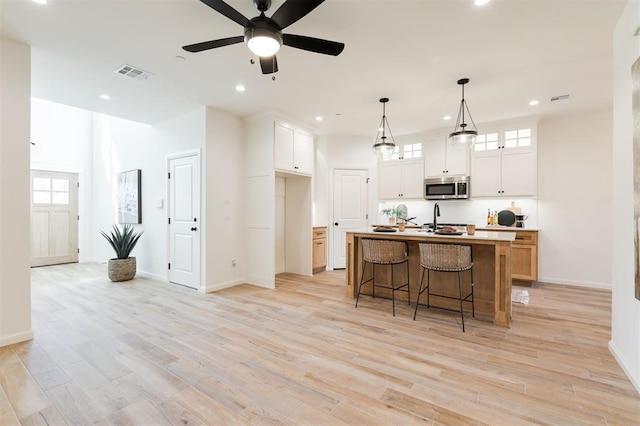 kitchen featuring light wood finished floors, stainless steel microwave, visible vents, white cabinetry, and a kitchen bar