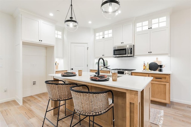 kitchen with light countertops, stainless steel microwave, light wood-style flooring, and an island with sink