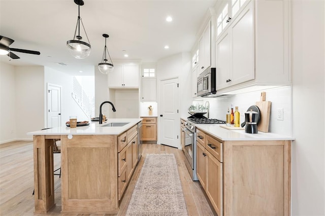 kitchen with tasteful backsplash, an island with sink, appliances with stainless steel finishes, light wood-type flooring, and a sink