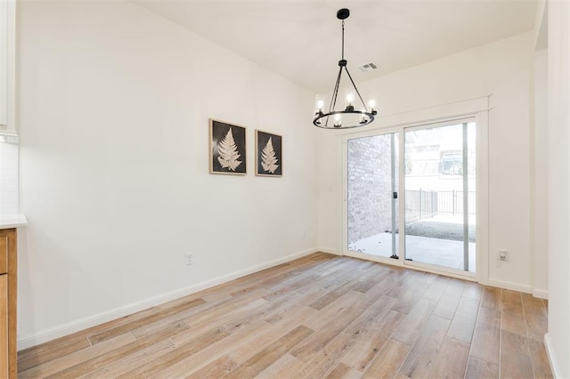 empty room with baseboards, light wood-type flooring, visible vents, and a notable chandelier