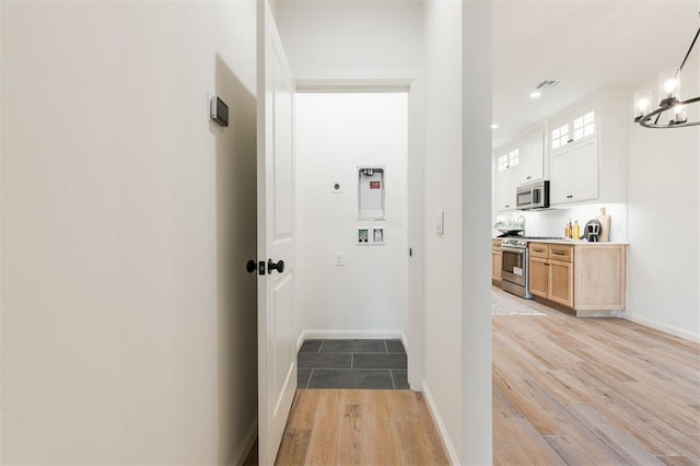 hall featuring baseboards, an inviting chandelier, visible vents, and light wood-style floors