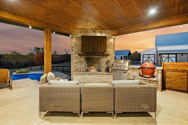 patio terrace at dusk featuring an outdoor brick fireplace, a grill, and area for grilling