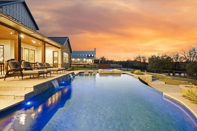 pool at dusk with an outdoor hangout area, a patio area, pool water feature, and an in ground hot tub