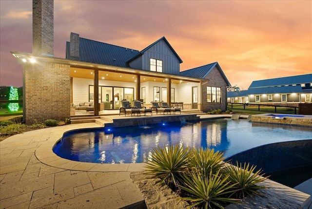 pool at dusk with an in ground hot tub and a patio