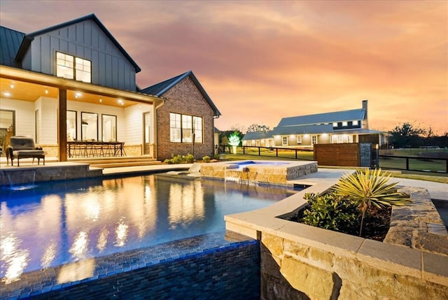 pool at dusk featuring an in ground hot tub, pool water feature, and a patio area