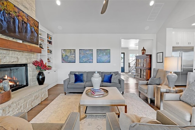 living room with a stone fireplace, hardwood / wood-style floors, built in features, and ceiling fan