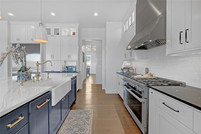 kitchen featuring sink, white cabinetry, appliances with stainless steel finishes, pendant lighting, and wall chimney range hood