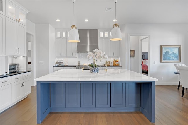 kitchen with pendant lighting, wall chimney range hood, white cabinetry, and a large island with sink