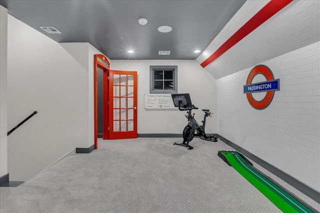 workout room featuring vaulted ceiling, light colored carpet, and brick wall