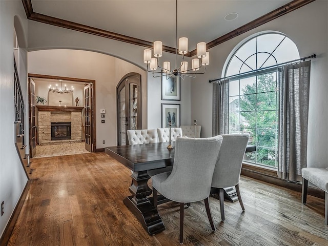 dining area featuring a notable chandelier, a stone fireplace, wood-type flooring, and ornamental molding