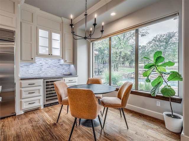 dining space featuring a healthy amount of sunlight, light hardwood / wood-style floors, beverage cooler, and an inviting chandelier