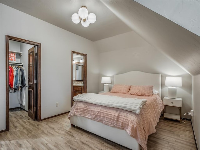 bedroom featuring a walk in closet, ensuite bath, vaulted ceiling, light hardwood / wood-style flooring, and a closet