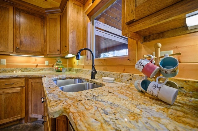 kitchen featuring light stone counters, sink, and wood walls