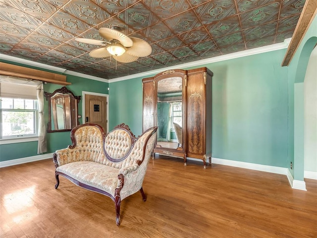 living area featuring ceiling fan, wood-type flooring, and crown molding