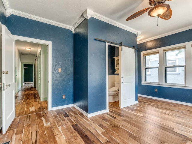 unfurnished bedroom featuring hardwood / wood-style floors, a barn door, ceiling fan, and crown molding