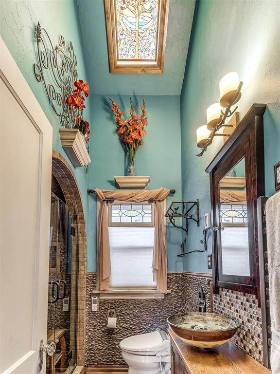 bathroom featuring vanity, toilet, a shower with shower door, and tile walls