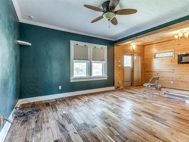 spare room with ceiling fan, wood-type flooring, crown molding, and wooden walls