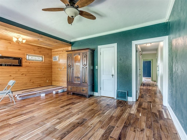 interior space featuring ceiling fan with notable chandelier, wood walls, wood-type flooring, and ornamental molding